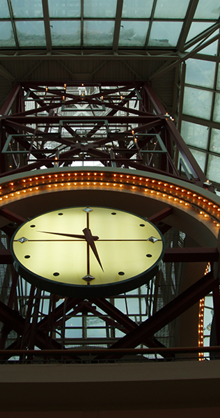 Illuminated Clock on a Steel Tower Leading to a Glass Ceiling
