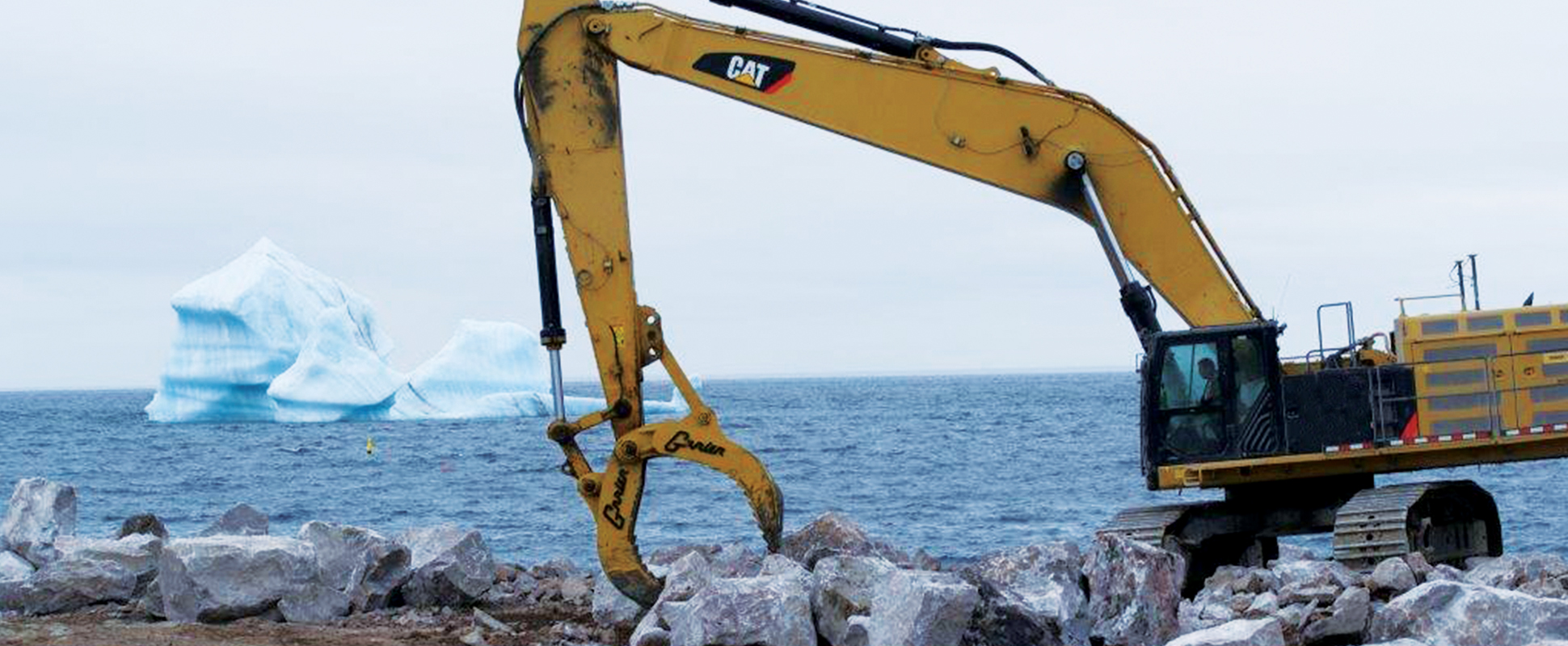 Machinery being operated at construction site with iceberg in background